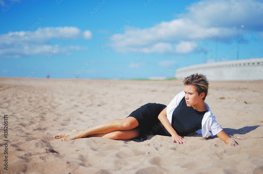 Outdoor street fashion style, young slim woman posing in fashionable dress on the beach, lying on sand Outdoor street fashion style, young slim woman posing in fashionable dress on the beach, lying on sand