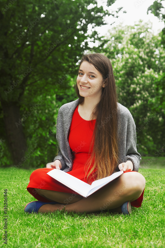 Obraz premium beautiful young girl siting on the grass and reading a book (edu