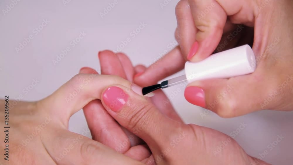 Woman cosmetician painting nails polish colorless varnish in beauty saloon, close up Woman cosmetician painting nails polish colorless varnish in beauty saloon, close up