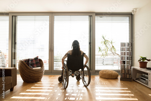 Young disabled woman in wheelchair at home, rear view. photo