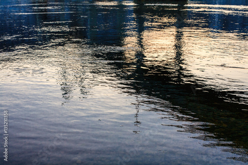 Blue river texture with bridge and sunset reflected in it