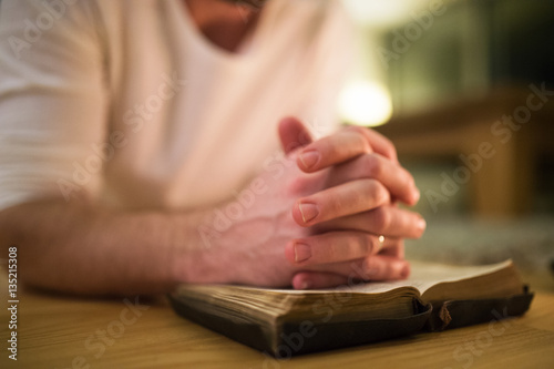 Unrecognizable man praying, kneeling on the floor, hands on Bibl