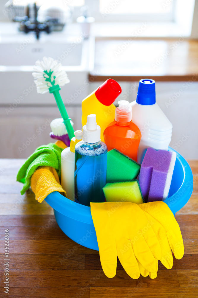 Basket with cleaning items on blurry background white citchen. Cleaning concept
