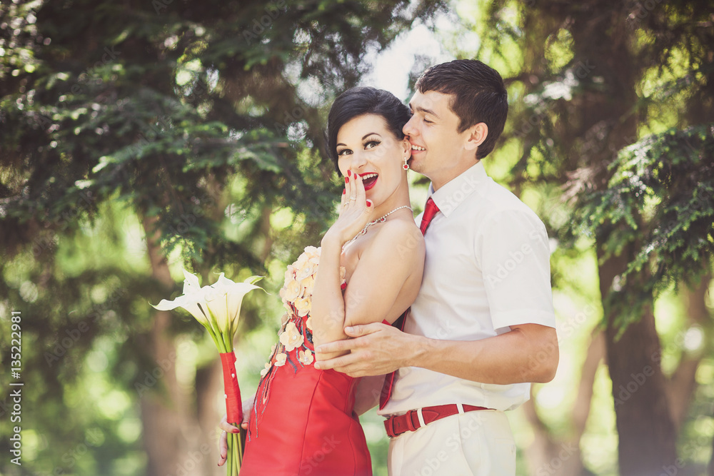 Obraz premium Groom with red tie hugs bride in red wedding dress