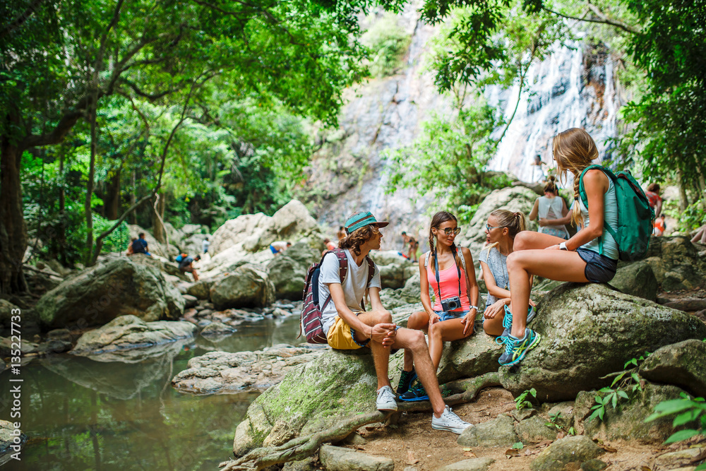 Obraz premium tourists sitting on rocks talking in front of jungle river with waterfall