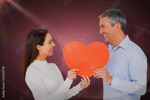Composite image of smiling couple holding heart shape paper