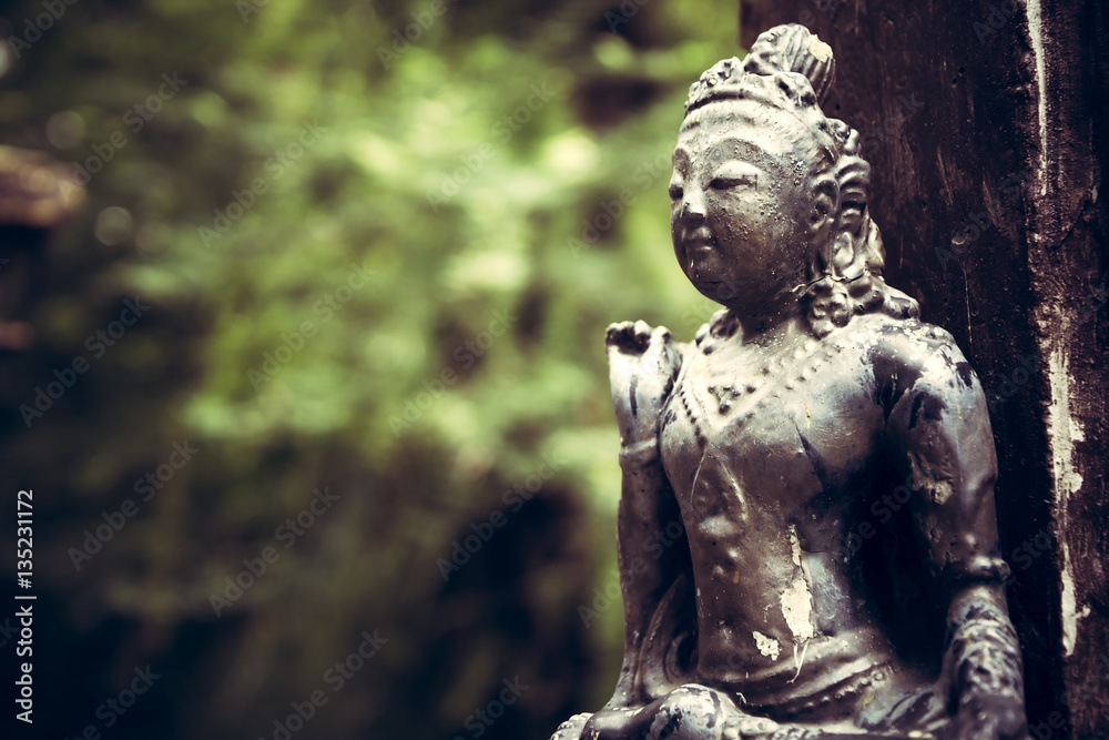 Old Asian style religious sculpture outdoors in the garden with blurred green forest background and copy space in vintage style Old Asian style religious sculpture outdoors in the garden with blurred green forest background and copy space in vintage style