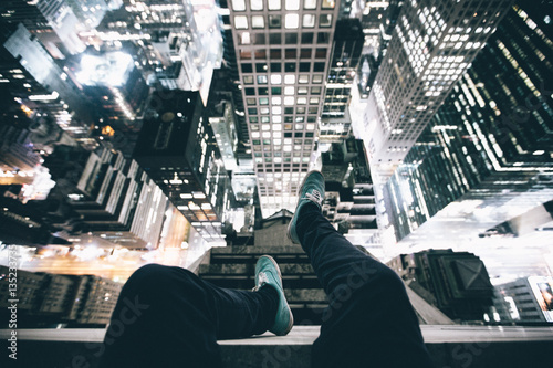 Point of view image of persons legs on top of skyscraper illuminated at night photo