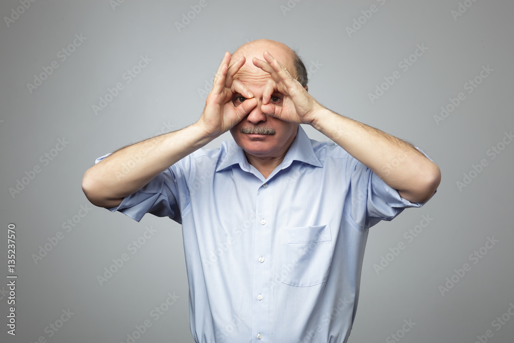 Old man holding fingers near eyes like glasses: mask like superhero Old man holding fingers near eyes like glasses: mask like superhero