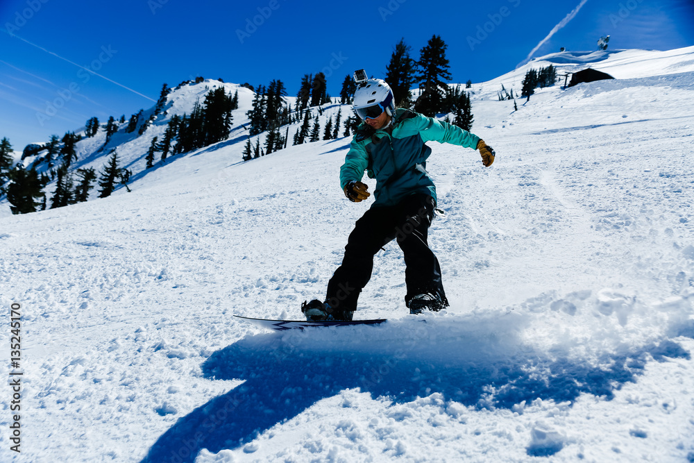 Young mixed race woman wearing teal jacket and white helmet snowboards on a clear blue day
