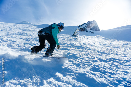 Young woman in teal jacket and white helmet snowboards down a steep mountain