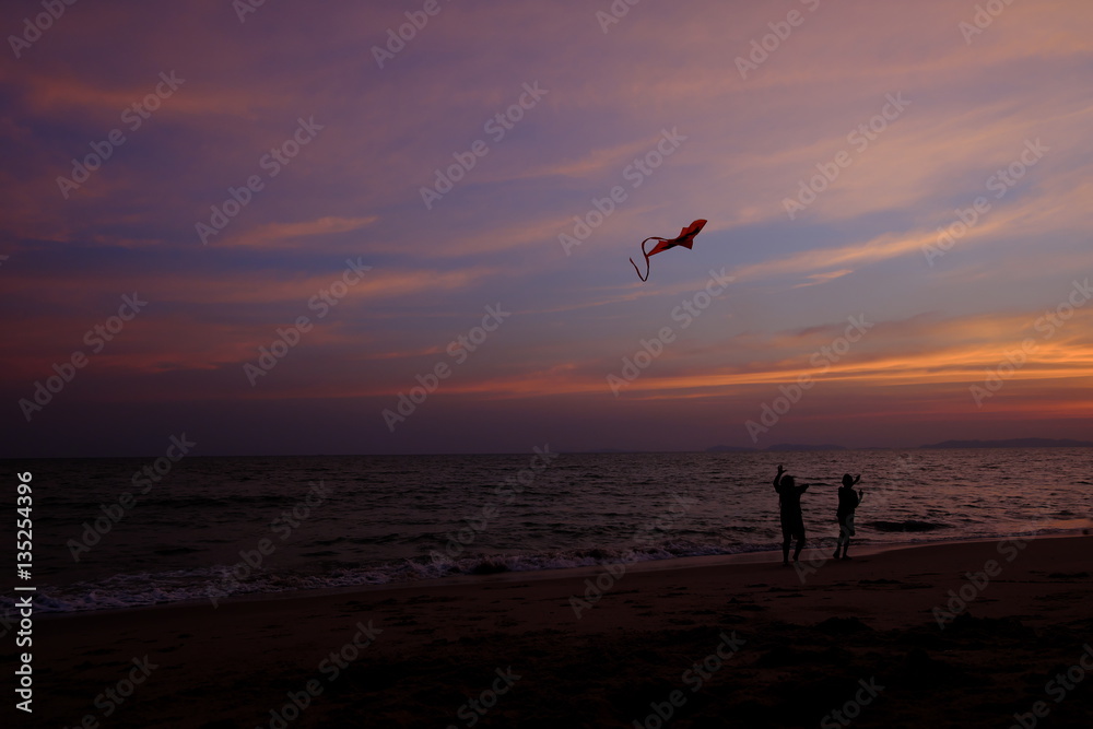 Boy and girl playing a kite on the beach. Twilight sky background.