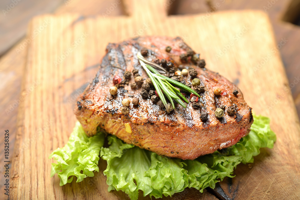Grilled beef steak with rosemary, salt and pepper on cutting board Grilled beef steak with rosemary, salt and pepper on cutting board