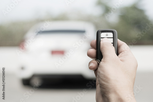 Hand of man holding and push remote control of car and white car parking background technology transportation safety concept