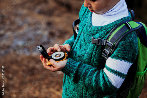 little boy travels with compass in green forest