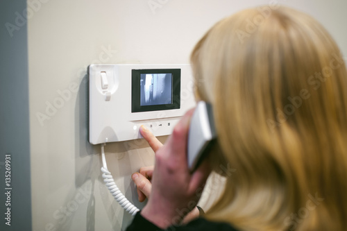 blonde woman hangs up the phone after answering the intercom call in her apartment photo