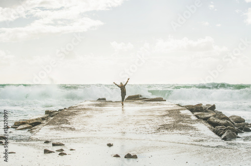 Young woman tourist enjoying waves of stormy Mediterranean sea in winter with raised hands, Alanya, Turlkey