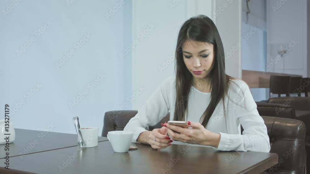 Beautiful young woman texting on smartphone in a cafe Beautiful young woman texting on smartphone in a cafe
