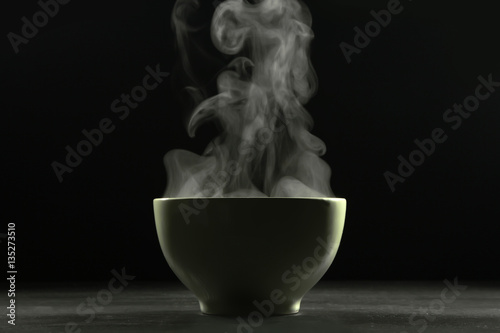 A bowl of hot food and steam on dark background.