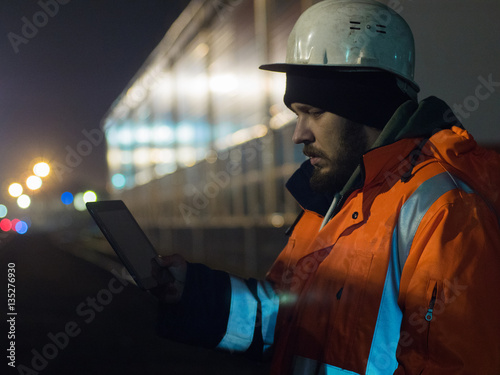 Portrait of young engineer working on tablet during hignt otdoors in helmet and reflective jacket