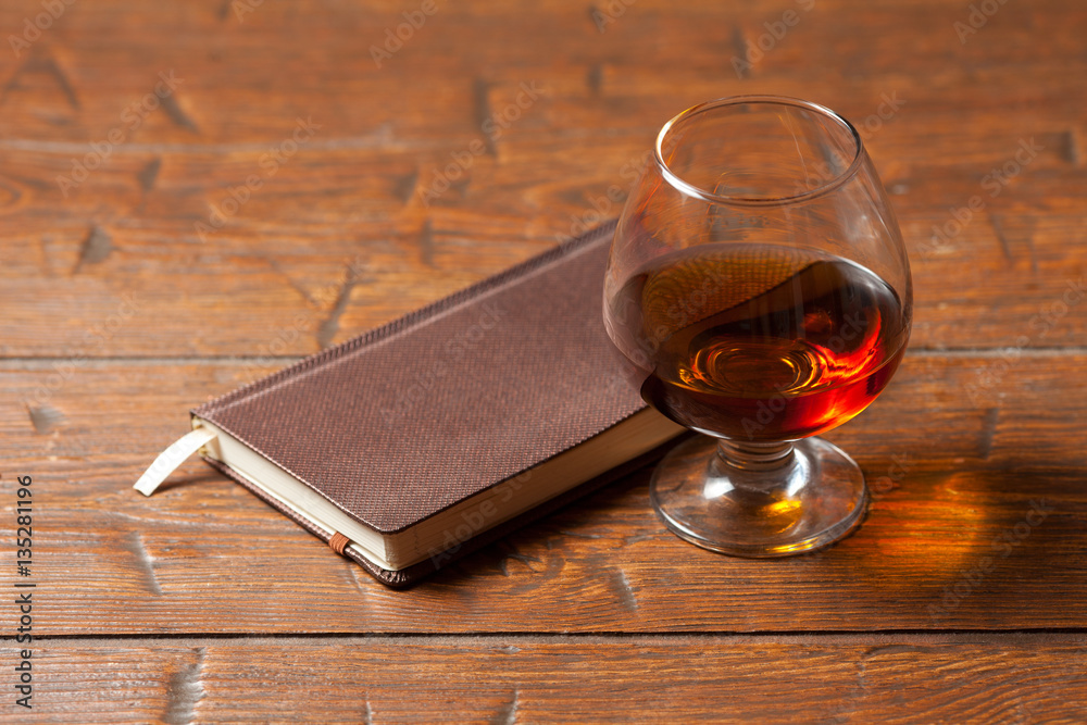 Glass of cognac, notebook on wooden background