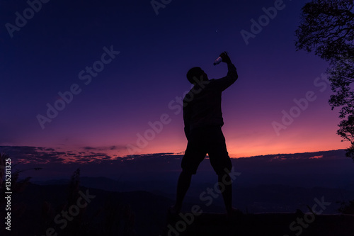 Silhouette of a man drinking happily at sunset.