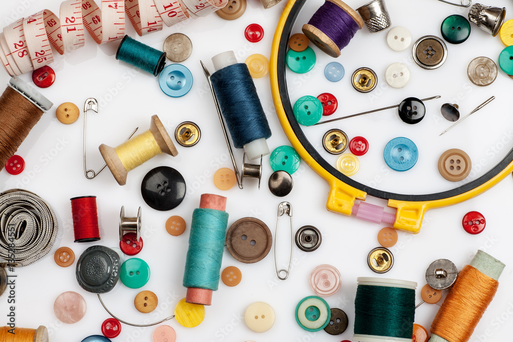 Threads, needles, buttons and other sewing stuff on a white background, flat lay composition, top view.