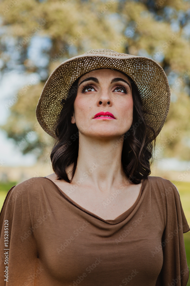 Stylish young woman with straw hat looking up