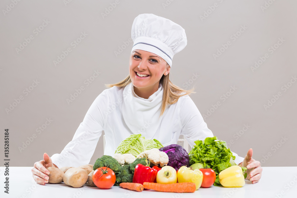 Cheerful female chef is sitting at the table with bunch of vegetable.
Cheerful female chef is sitting at the table with bunch of vegetable.