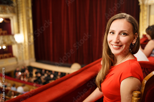 Young smiling woman in red dress sitting on balcony in the theatre