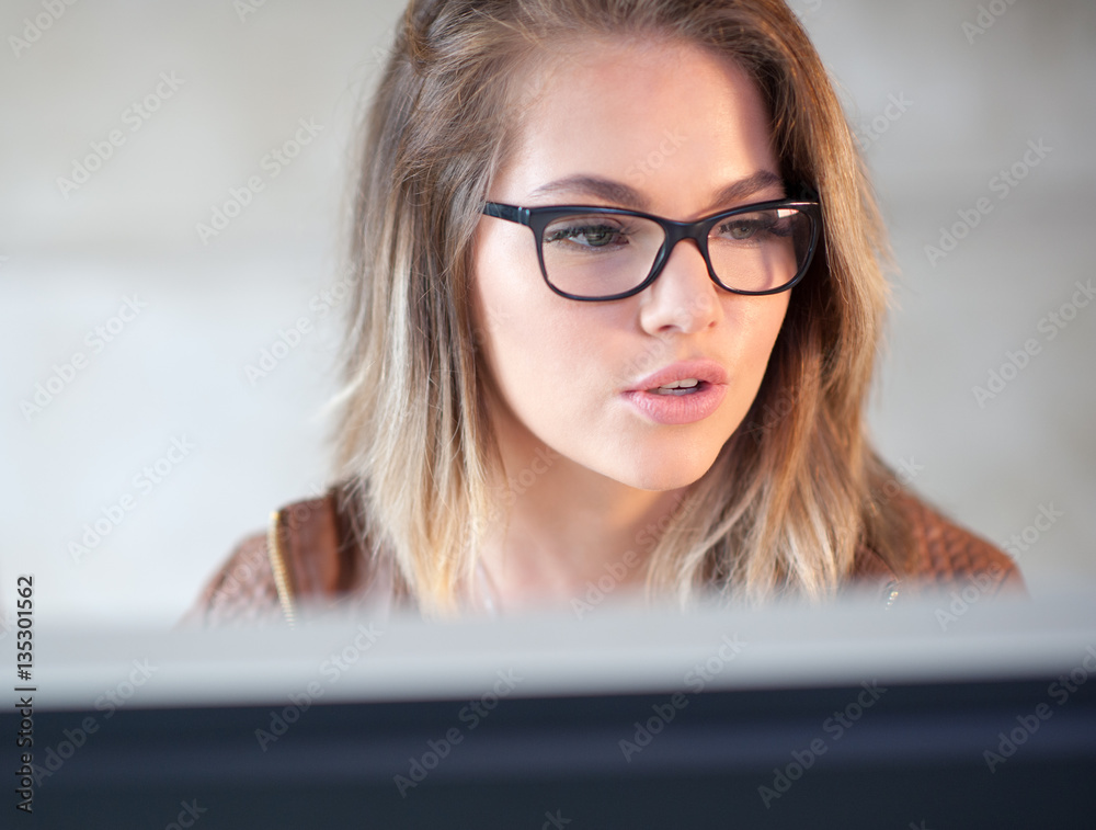 Beautiful young woman sitting at her desk working on a computer. Beautiful young woman sitting at her desk working on a computer.