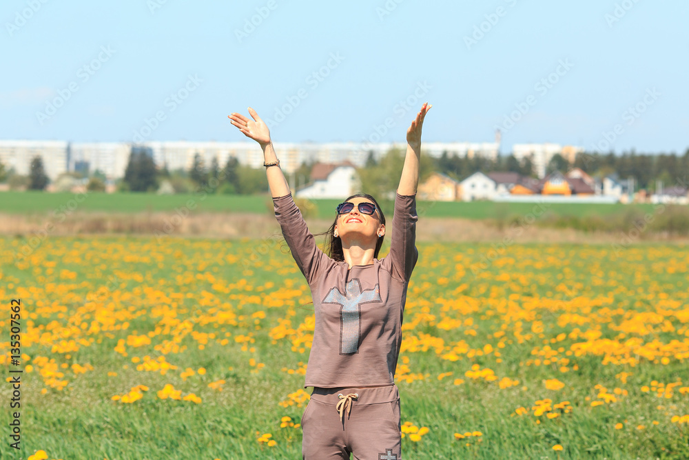 Young beautiful white girl in a brown sports suit stands in a field of yellow dandelions. Spring portrait. Young beautiful white girl in a brown sports suit stands in a field of yellow dandelions. Spring portrait.