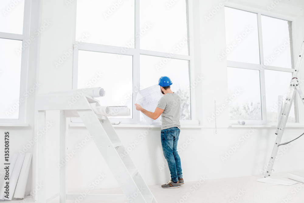 White interior for renovation and repair with ladder, windows and foreman or builder looking at paper drawings
