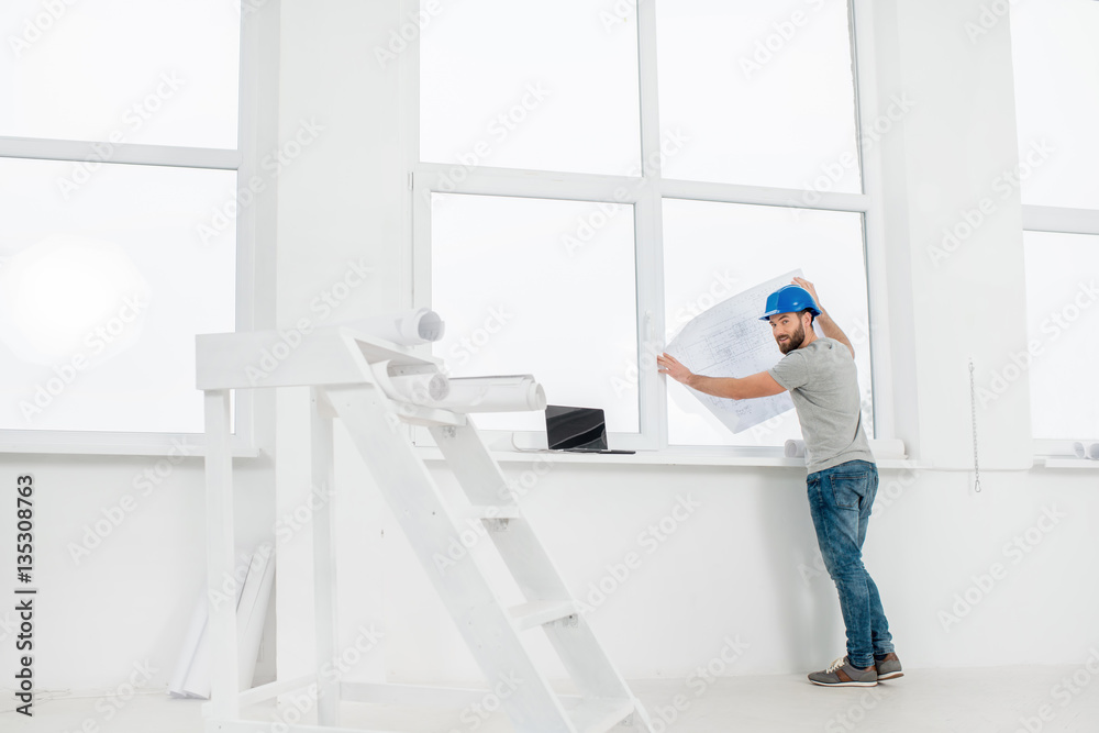 White interior for renovation and repair with ladder, windows and foreman or builder looking at paper drawings