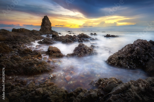 Seascape of sea with dramatic wave and rock in sunset.