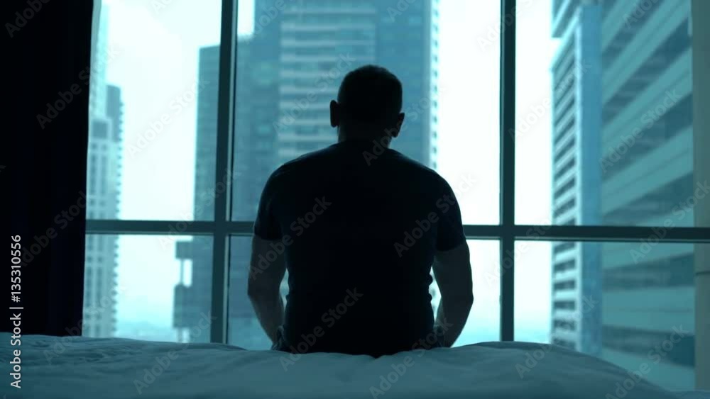 Silhouette of lonely man admire view sitting on bed at home

