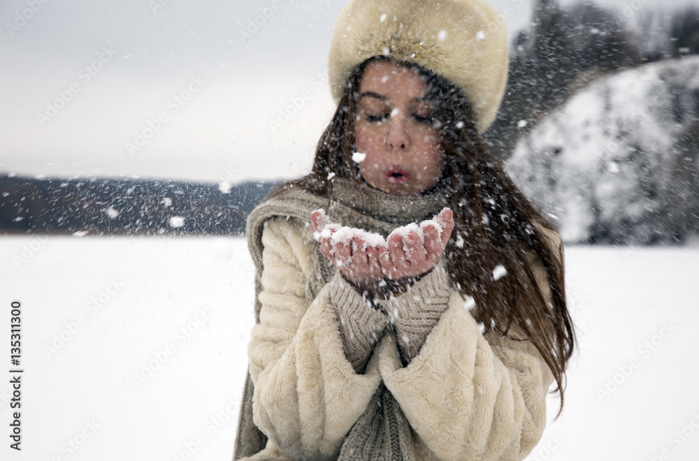 Fototapeta premium The girl with dark hair in a bright sheepskin playing in the snow on a background of a winter landscape painting