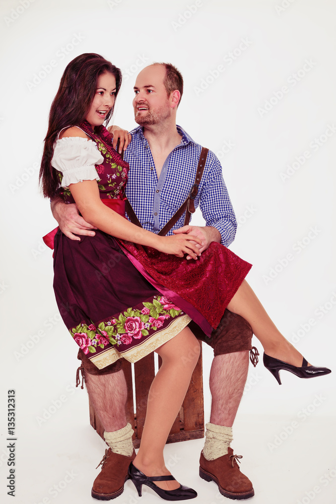 Junge Frau sitzt beim Mann auf dem Schoß. Bayerische Pärchen in Dirndl und Lederhose isoliert
