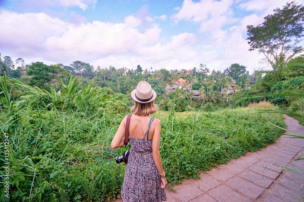 Tourism and travel. Young woman in hat with camera walking on path, enjoying beautiful view.