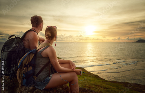 Couple hikers with backpacks enjoying sunrise on top of a mounta