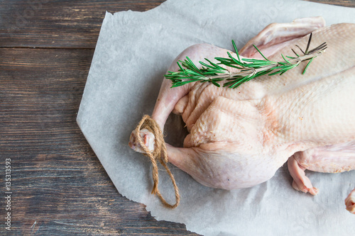 Raw duck meat - whole bird - on paper with rosemary