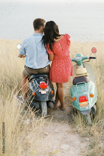 Happy young couple in love on retro motorbike driving togetger and ejoying the trip near the ocean. photo