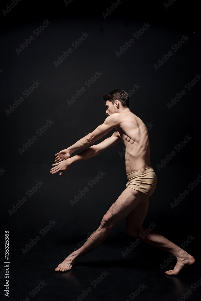 Powerful young man dancing in the black colored studio