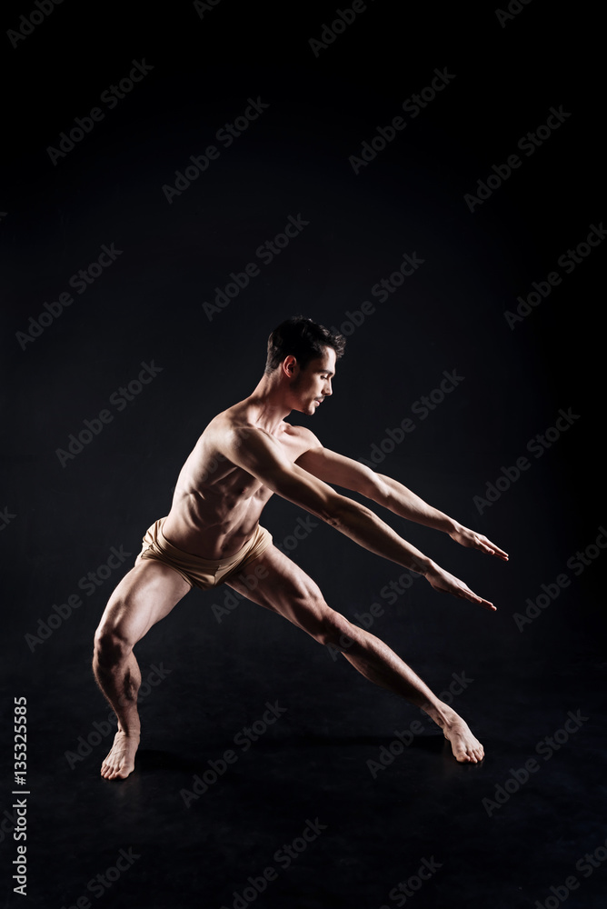 Attentive sportsman balancing in the dark lighted studio Attentive sportsman balancing in the dark lighted studio