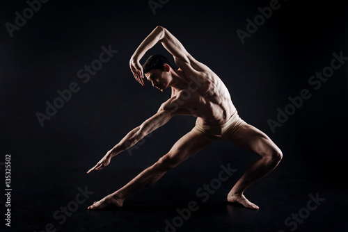 Athletic man doing yoga in the black colored studio