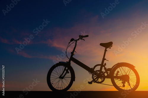 Silhouette bicycle on dramatic sky at sunset.