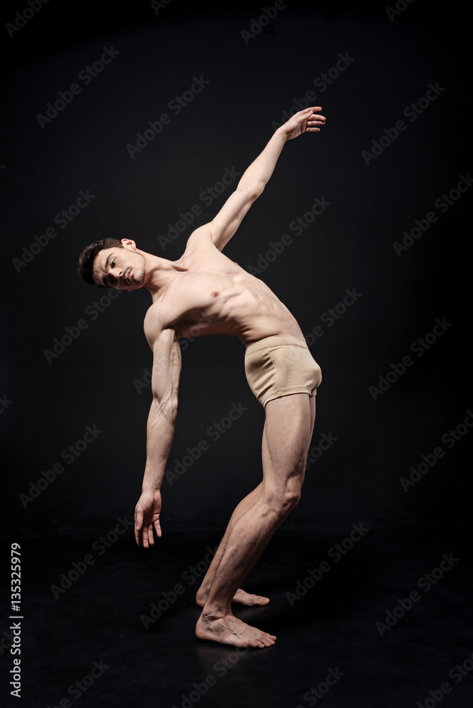 Peaceful young gymnast performing in the dark lighted studio
