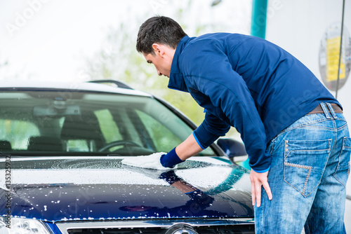Hard-working man polishing car with white microfiber mitt