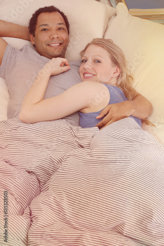 Couple cuddling in bed in a Sunday morning