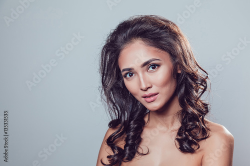 Brunette girl with shiny wavy hair and beautiful make up posing at studio on grey background.